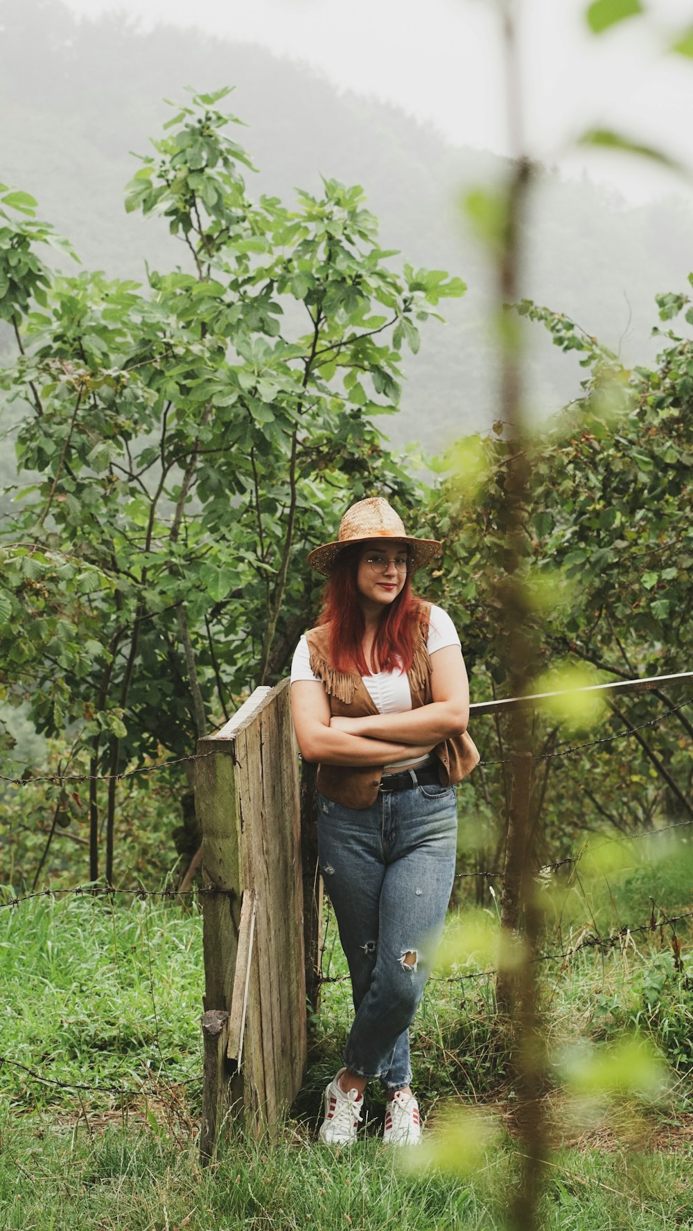 a woman in a hat leaning on a fence