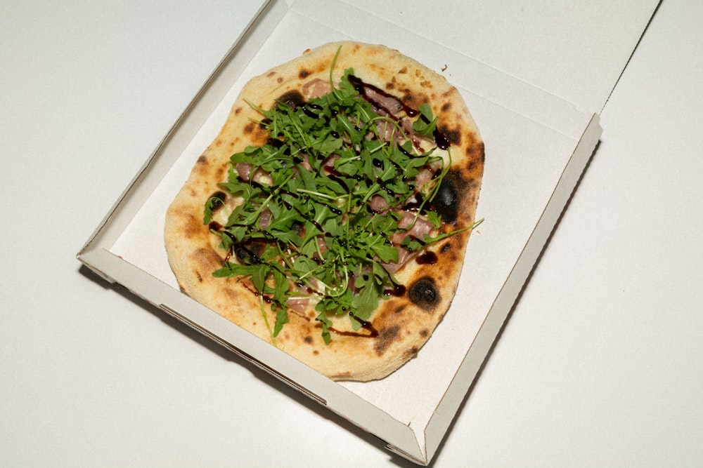 a pizza in a box with greens on top