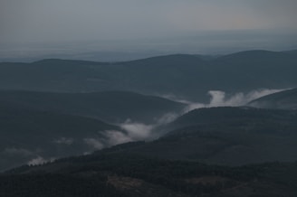 A vast, misty mountain range unfolding under a cloudy sky, showcasing rugged terrain.