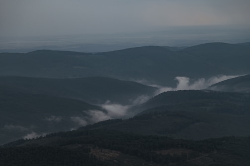 A vast, misty mountain range unfolding under a cloudy sky, showcasing rugged terrain.