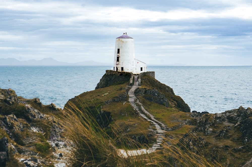 a white lighthouse sitting on top of a hill next to the ocean