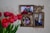 A decorative photo frame with three pictures is displayed on a textured wall. The frame features intricate designs with birds and leaves, and is made of a bronze or gold-colored material. To the left of the frame is a bouquet of bright red tulips with green stems.
