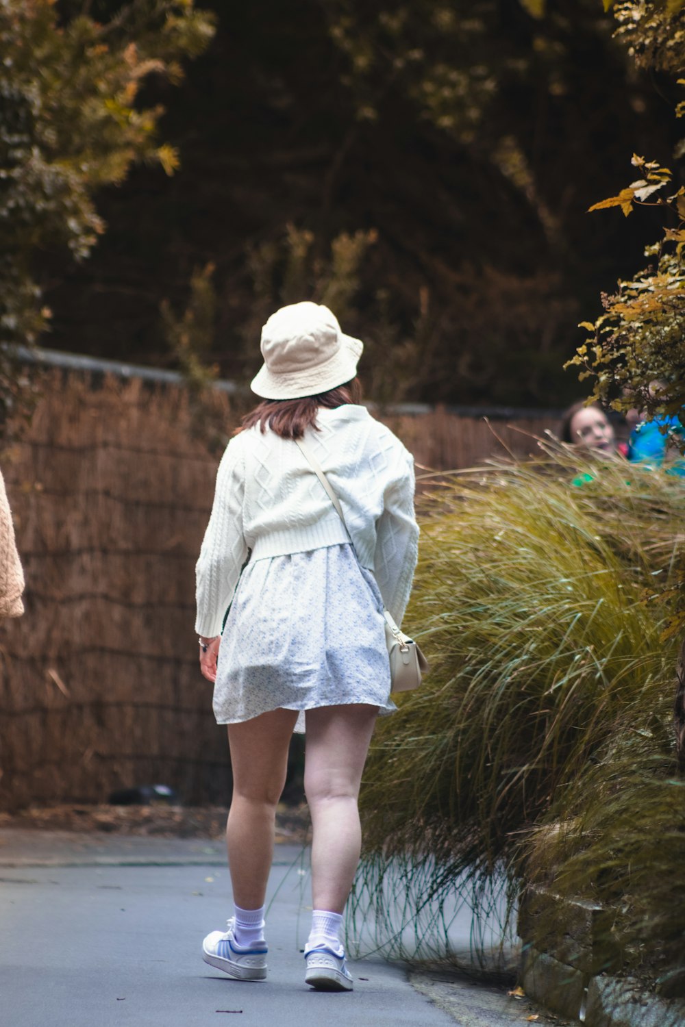 a woman walking down a sidewalk in a white dress