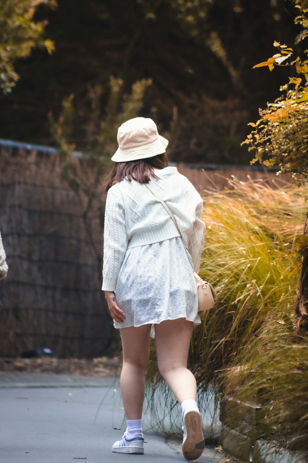 a woman in a white dress and hat walking down a sidewalk