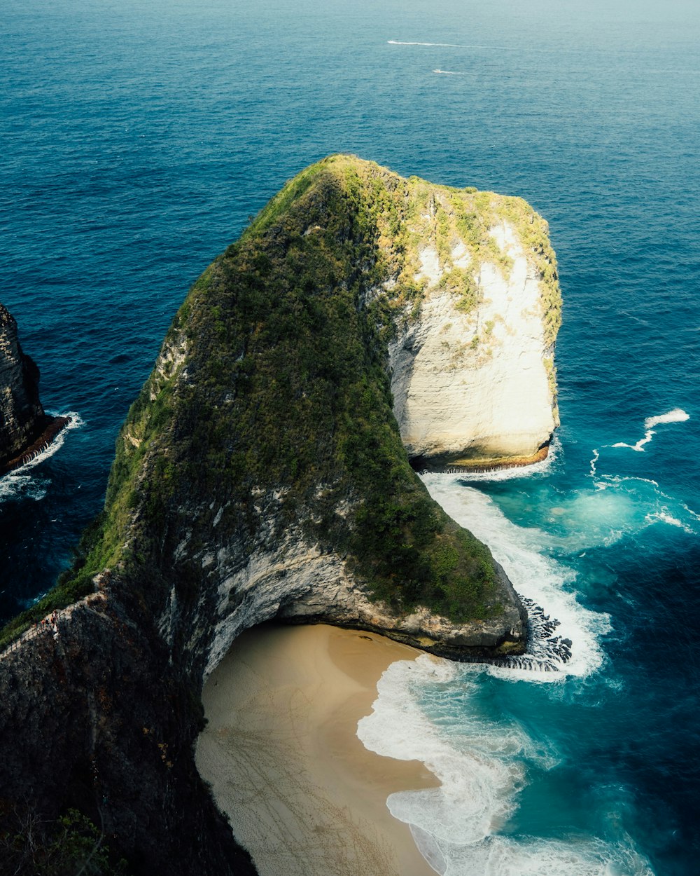 a large rock sticking out of the ocean next to a beach