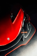 Close-up of a sleek black car with red accents and carbon fiber texture shining under soft lighting.