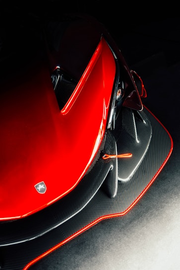 Close-up of a sleek black car with red accents and carbon fiber texture shining under soft lighting.
