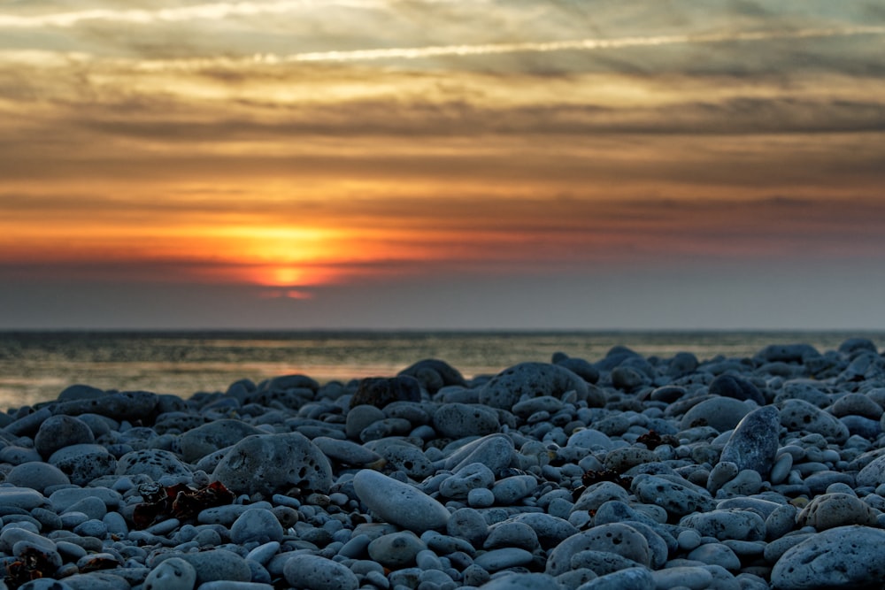 the sun is setting over a rocky beach