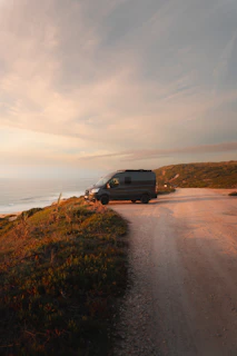 Golden hour light bathes a winding mountain road with a sleek tour van parked beside it