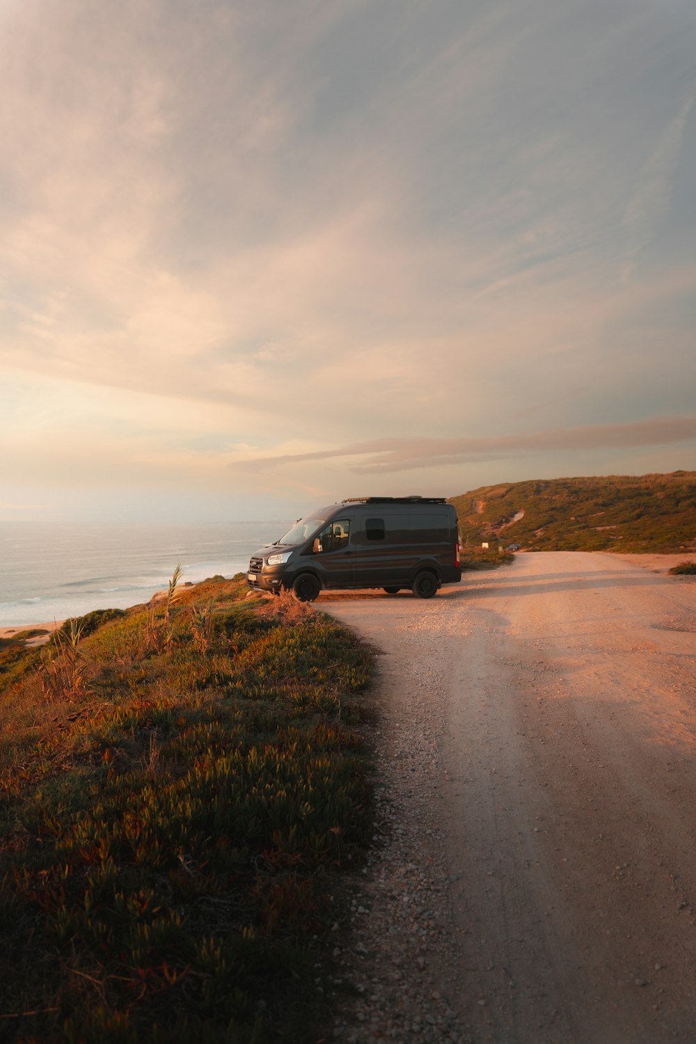 a van driving down a dirt road next to the ocean