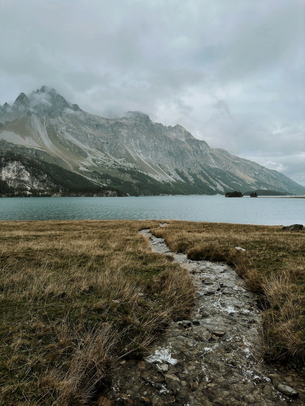 a path leading to a body of water with mountains in the background