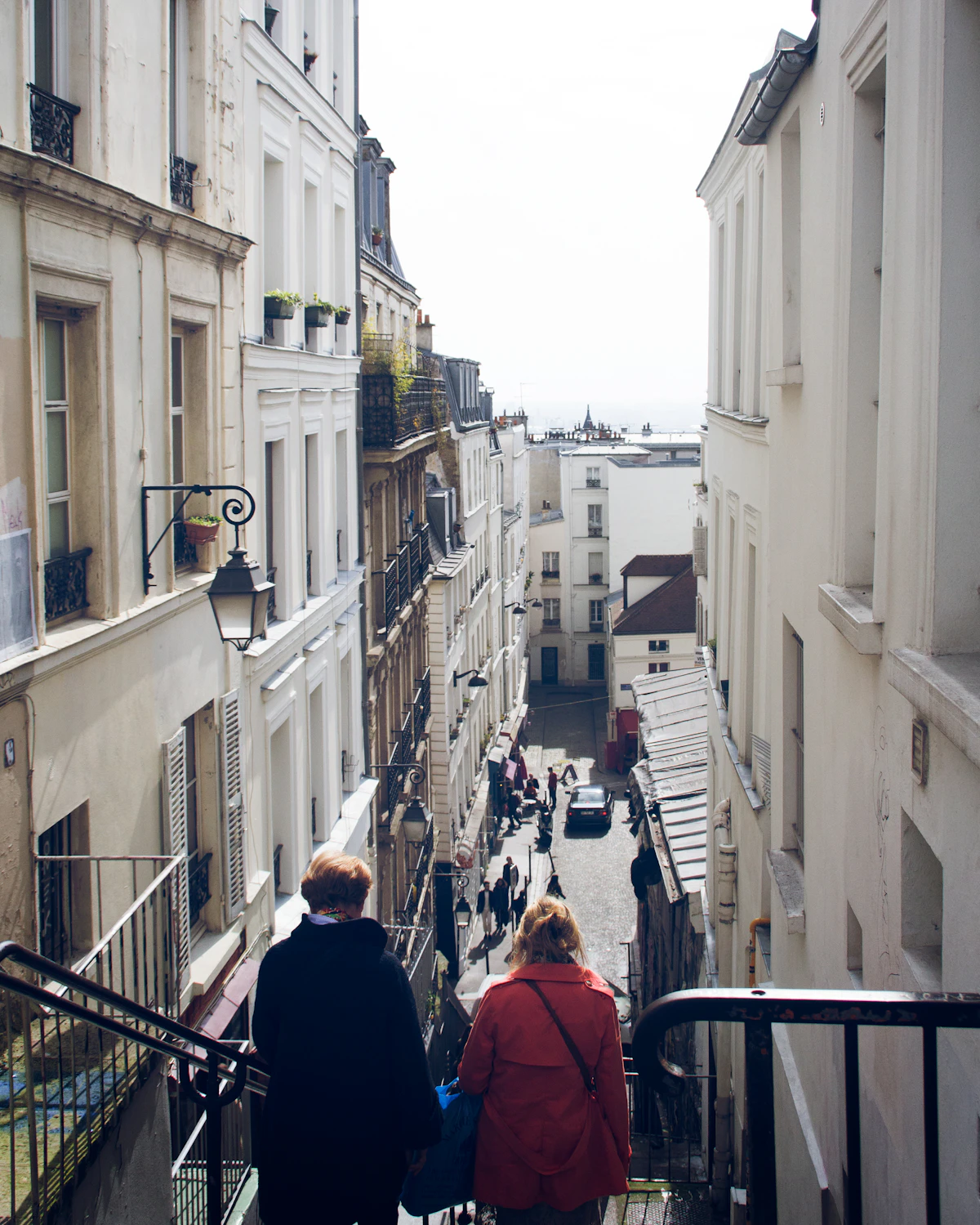 Steps going down between the façades of Montmartre, two people seen from behind