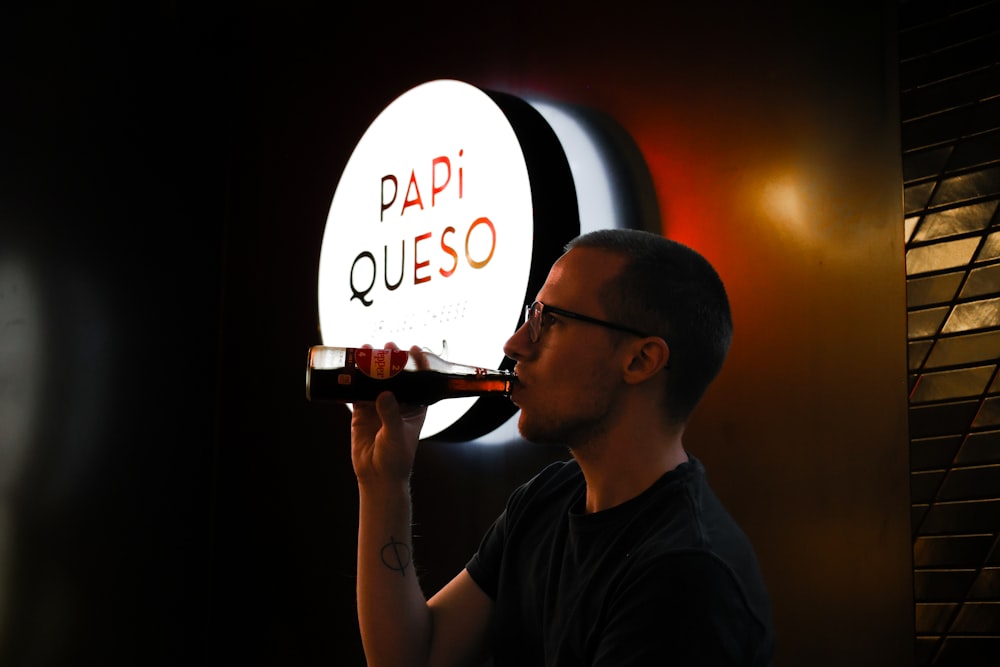 a man drinking from a bottle in front of a sign
