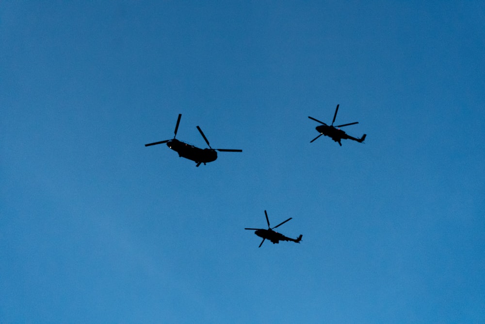 three military helicopters flying through a blue sky