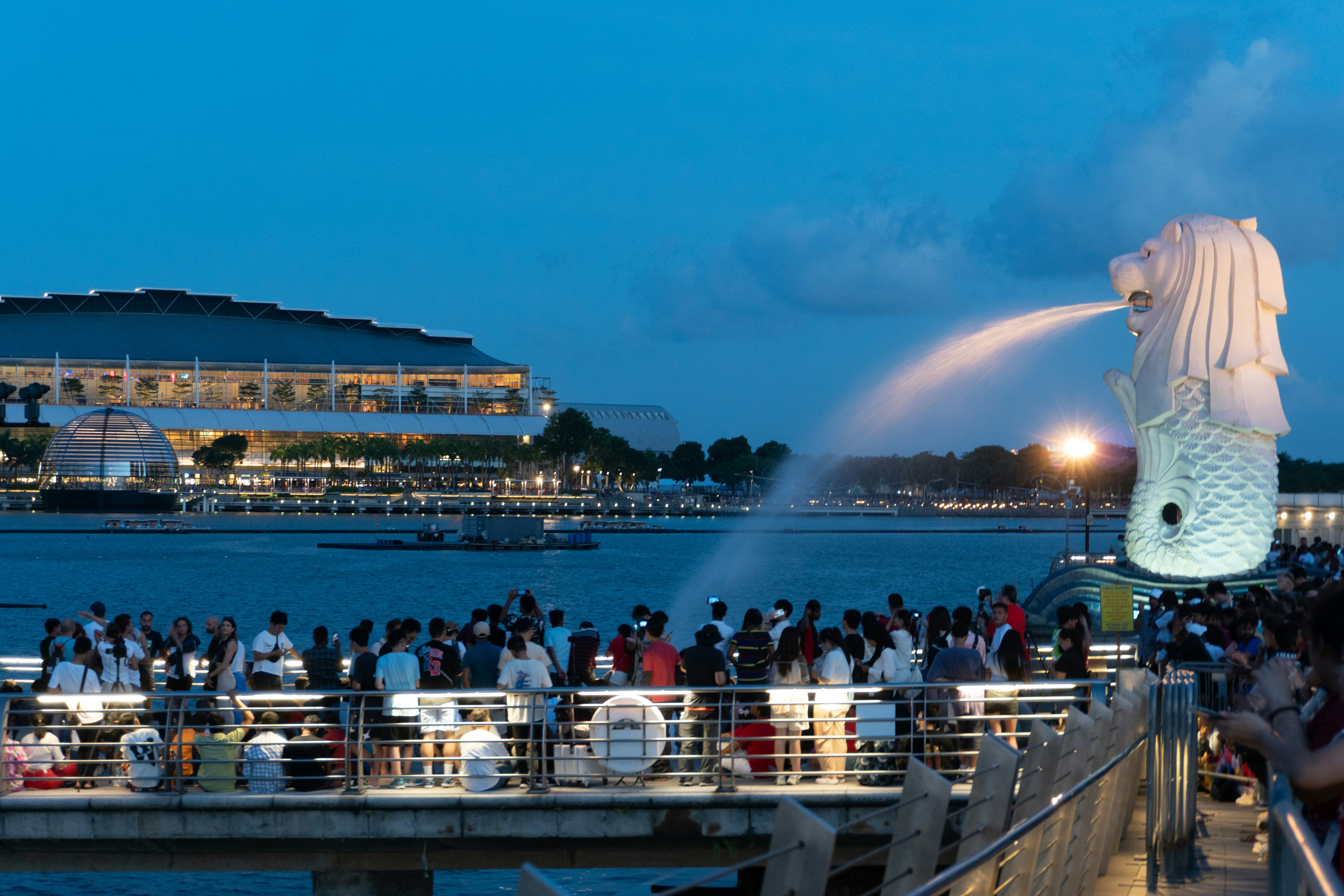 a crowd of people standing on a pier next to a large statue