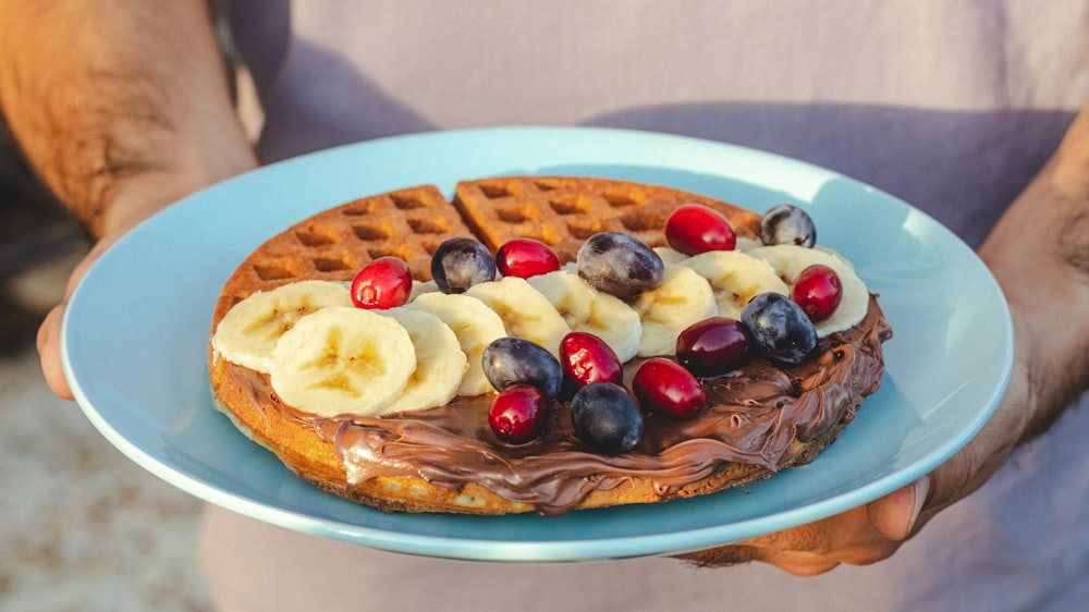 a person holding a plate with waffles and fruit on it