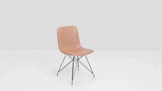 A tan molded plastic chair with a minimalist design sits on black metal legs with cross-bracing. The background is a simple light gray, enhancing the chair's modern aesthetic.