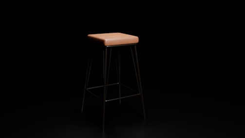 A sleek, modern stool with a square, light brown seat and thin, dark metal legs. The stool stands alone against a plain, dark background, accentuating its minimalist design.