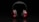 A pair of over-ear headphones with red ear cups and black padding, placed against a dark background. The lighting highlights the sleek design and vibrant color contrast.