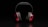 A pair of over-ear headphones with red ear cups and black padding, placed against a dark background. The lighting highlights the sleek design and vibrant color contrast.