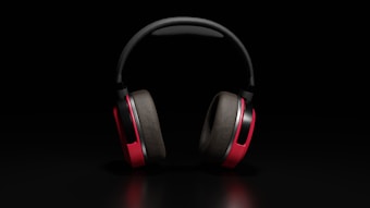 A pair of over-ear headphones with red ear cups and black padding, placed against a dark background. The lighting highlights the sleek design and vibrant color contrast.