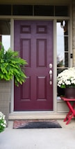 A welcoming front porch adorned with tropical plants and a bright mango-colored door.