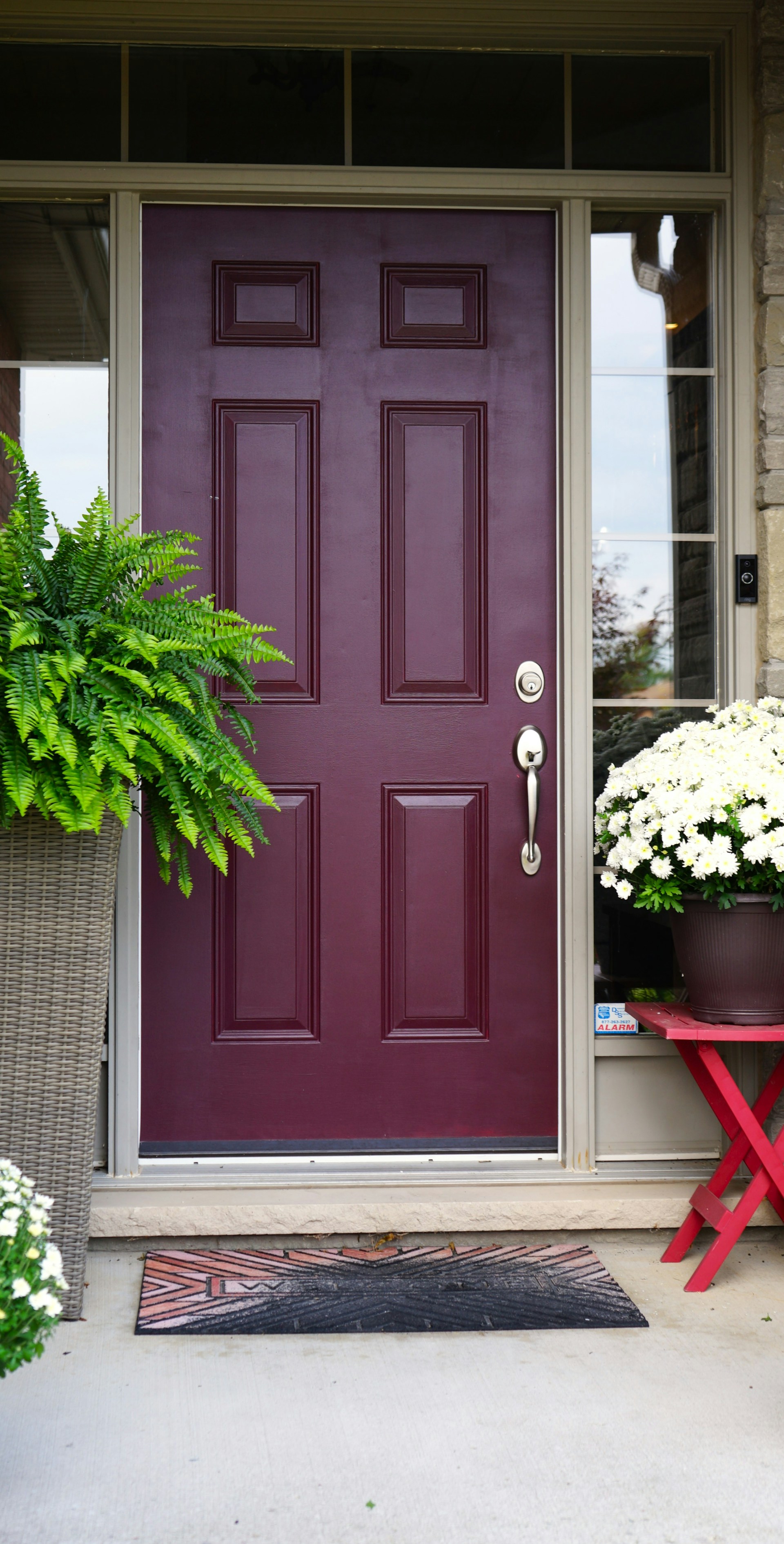 An inviting front door painted in vibrant red, surrounded by lush green plants and a welcoming porch.