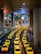 A long line of bright yellow taxis waits in orderly rows beneath a high, industrial ceiling. The setting appears to be a modern transportation hub, with multiple levels observed in the background. The scene is well-lit, creating a vibrant and bustling atmosphere.