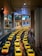 A long line of bright yellow taxis waits in orderly rows beneath a high, industrial ceiling. The setting appears to be a modern transportation hub, with multiple levels observed in the background. The scene is well-lit, creating a vibrant and bustling atmosphere.