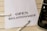 A white piece of paper laid on a wooden surface with the words 'OPEN RELATIONSHIP' printed on it. A fountain pen with a silver and black design is placed near the paper. Part of a typewriter is visible on the right side.
