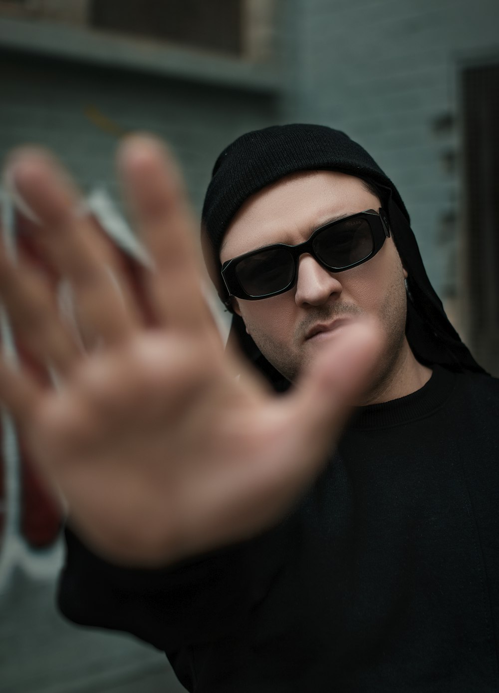 a man wearing sunglasses and a black hoodie making a hand gesture