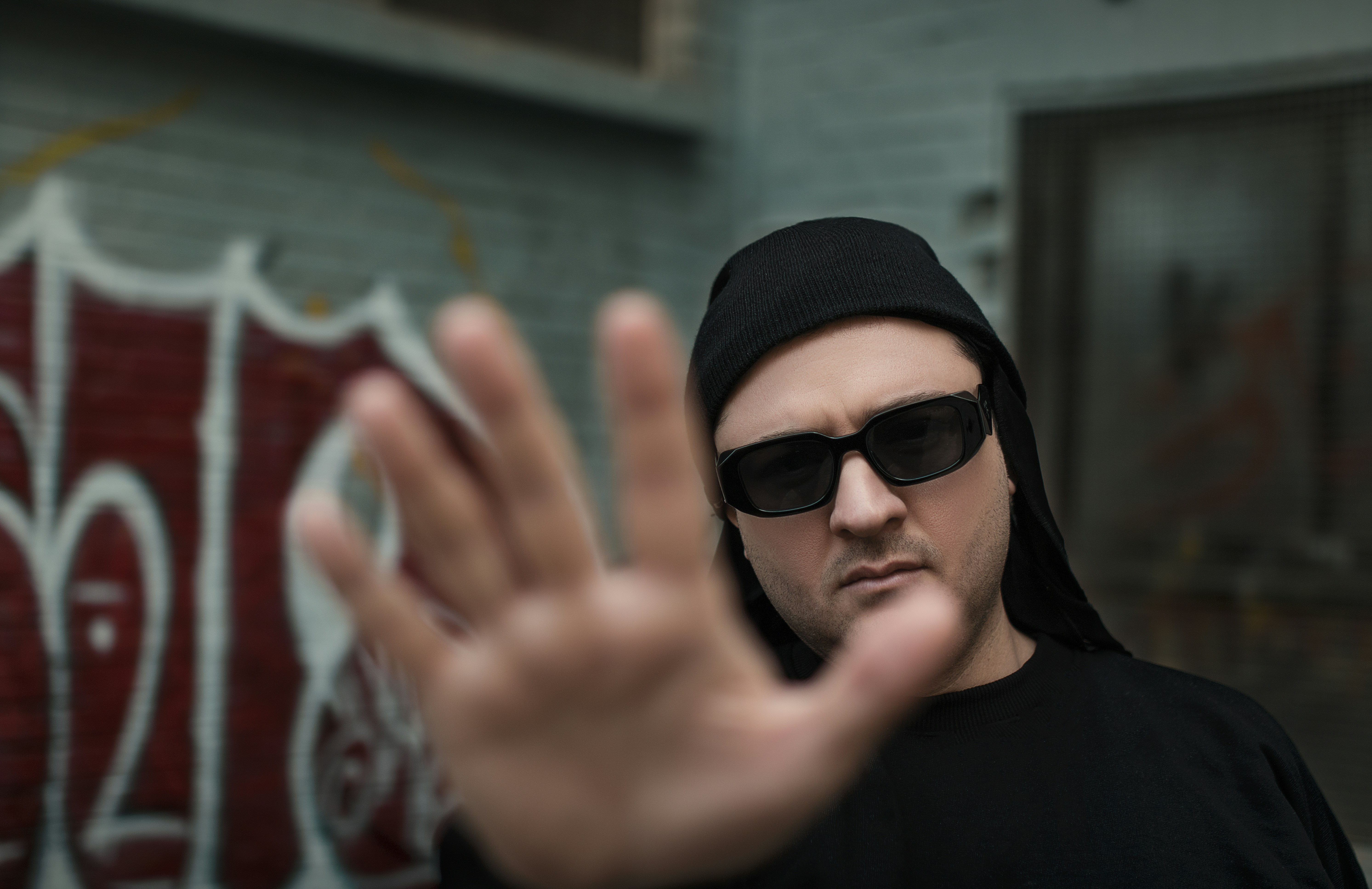 a man wearing sunglasses and a black hat making a hand gesture