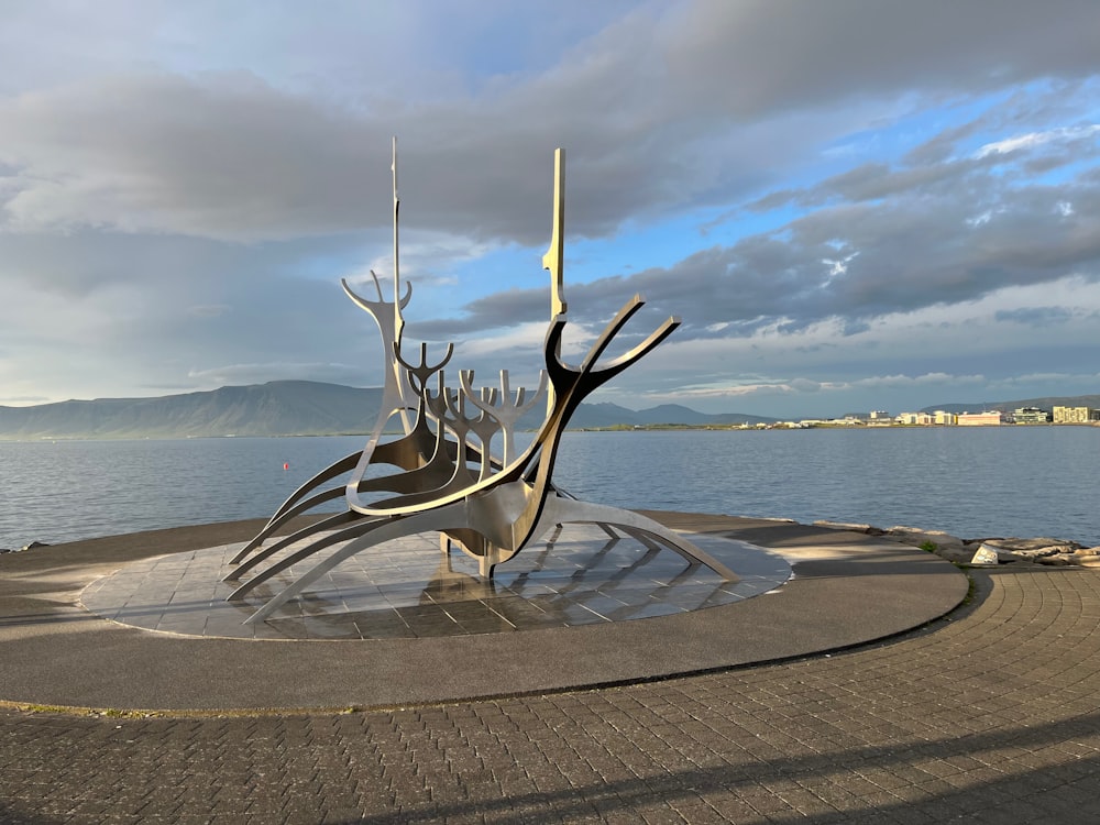 a large metal sculpture sitting in front of a body of water