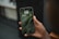 A hand holds a smartphone displaying the lock screen showing the time as 1:11 on Tuesday, 9 May, with a background of green leaves.
