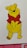 A yellow cartoon bear with a red shirt stands with a cheerful expression. The character has small ears, black eyes, a nose, and a friendly smile. The background is white with a partial view of a red and pink floral pattern at the bottom edge.