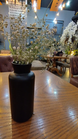 A bold, sculptural vase with a matte black finish sitting on a rustic wooden table.