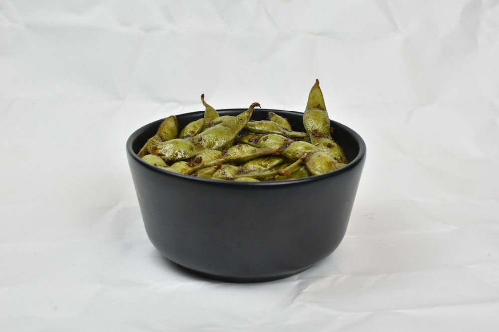 a black bowl filled with green beans on a white background