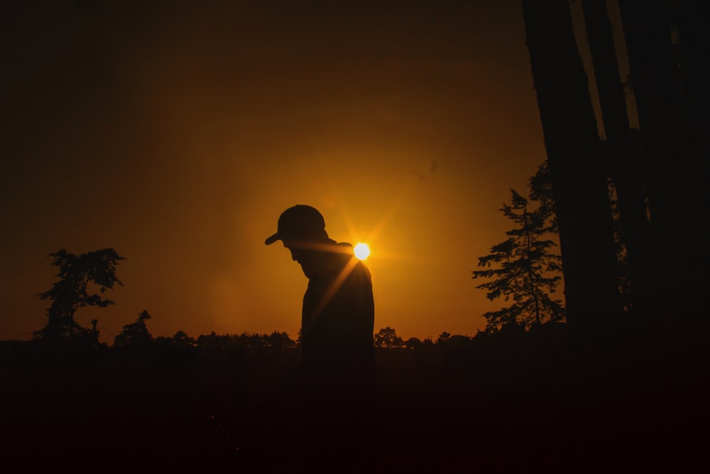 a person standing in the dark with the sun setting in the background