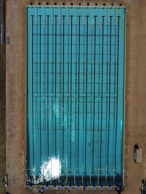 An Olympic-sized swimming pool with clear blue water and lane markings under a bright sky.