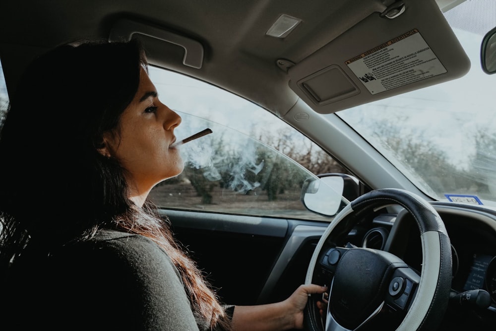a woman driving a car with a cigarette in her mouth