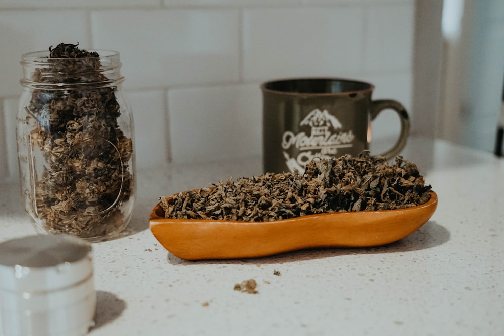 a bowl of dried herbs sitting on a counter next to a mug