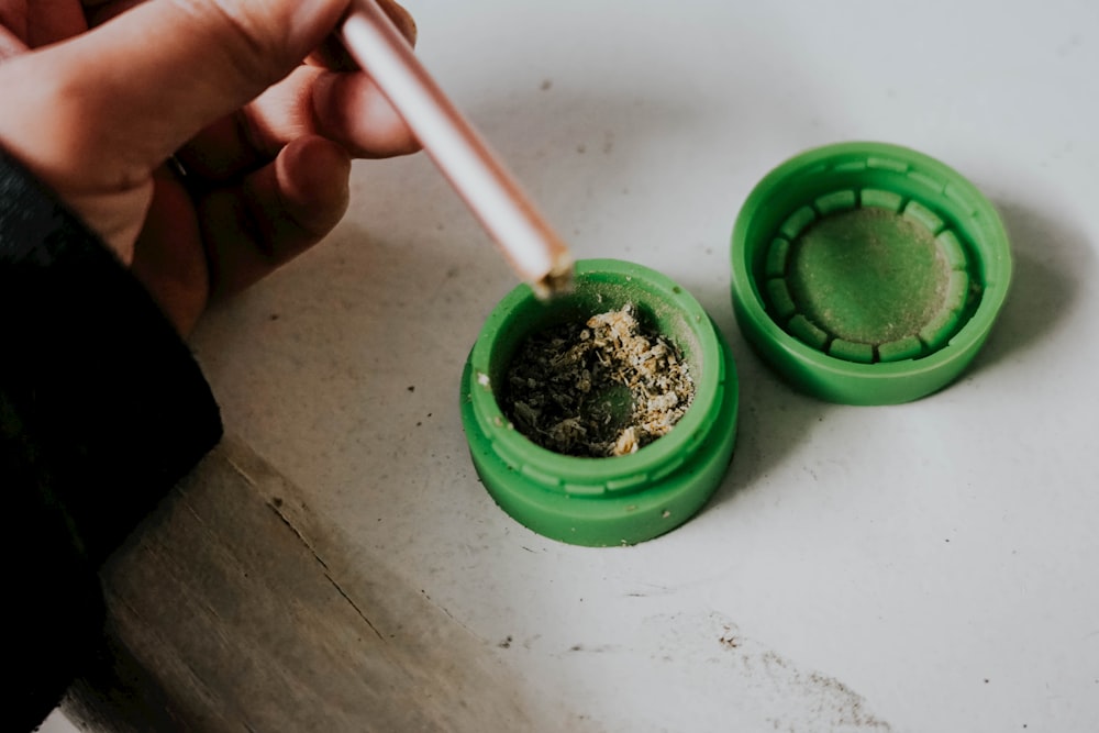 a person holding a brush over a green container