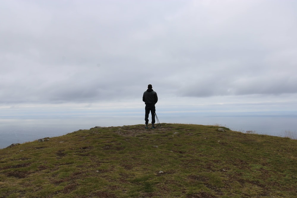 a man standing on top of a grass covered hill