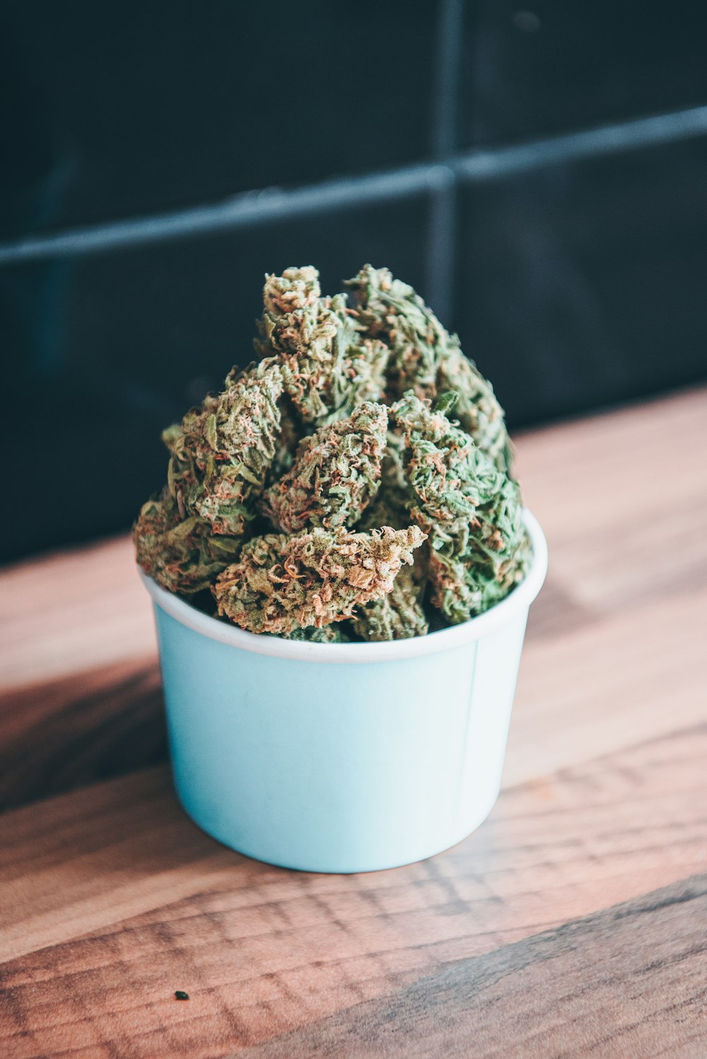 a blue bowl filled with green weed sitting on top of a wooden table