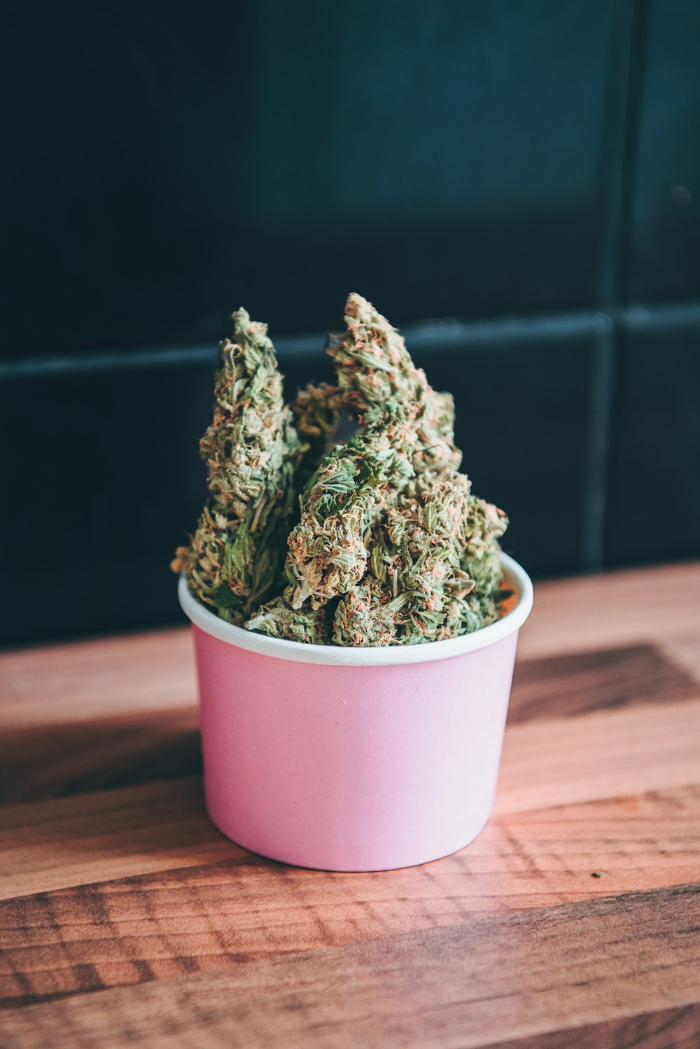 a pink bowl filled with marijuana sitting on top of a wooden table