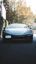 A clean, shiny car parked in a sunlit driveway surrounded by greenery.