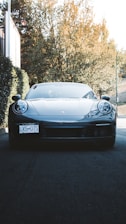 A clean, shiny car parked in a sunlit driveway surrounded by greenery.