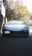 A clean car parked in a sunlit driveway surrounded by greenery.