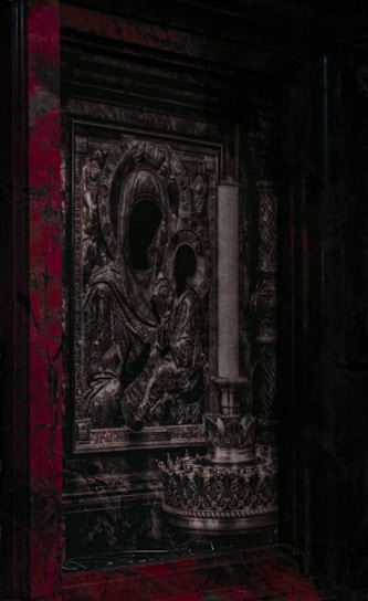 An intricately designed religious icon featuring figures with darkened faces, surrounded by ornate patterns and textures. Adjacent is a tall, decorative candle holder. The overall style appears to be historical and baroque, set against a backdrop with rich, dark colors.