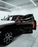 A luxury car is parked in a modern showroom with bright overhead lighting. The driver’s door is open, revealing a vibrant orange interior. The car's exterior features a sleek, black-and-white design with distinctive rims.